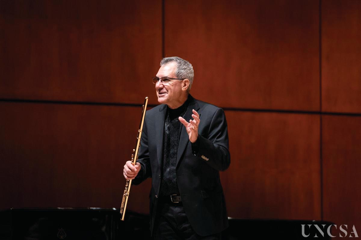 Tadeu Coelho speaking to an audience, flute in hand